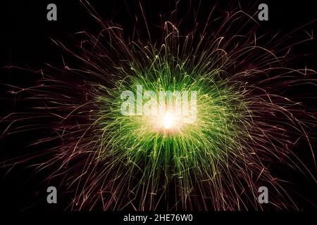 Rote und grüne Funken eines festlichen Neujahrslichts. Funken fliegen in verschiedene Richtungen vom brennenden Funker. Stockfoto