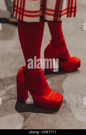 Damenbeine in roten Strumpfhosen und seidigen High Heels. Vertikale Modeaufnahme