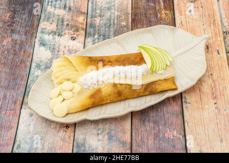 Französisches Crepe Dessert gefüllt mit Banane und Apfel mit weißer Schokolade und geriebener Kokosnuss Stockfoto