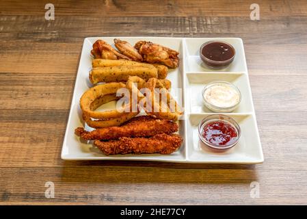 Kombination aus tex mex Snacks mit Chicken Strips, Zwiebelringen, Käsefingern und frittierten Flügeln mit verschiedenen Dipping-Saucen Stockfoto