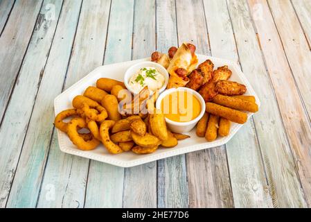 Eine Kombination aus verschiedenen Snacks mit Zwiebelringen, Kroketten, Pommes frites, Käsefinger, Hähnchenflügel und Würstchen mit verschiedenen Saucen Stockfoto