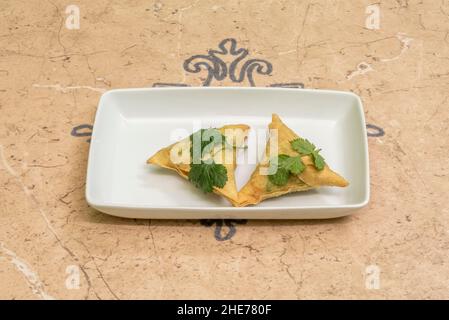 Samosa ist ein gebratener oder gebackener Knödel mit herzhafter Füllung, wie z. B. würzige Kartoffeln, Zwiebeln, Erbsen, Fleisch oder Linsen. Es kann verschiedene Formen annehmen, einschließlich Stockfoto