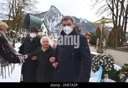 Oberammergau, Deutschland. 09th Januar 2022. Markus Söder, Bayerischer Ministerpräsident (CSU, r), unterstützt Max Streibls Witwe Irmingard Streibl neben ihrem Sohn Florian Streibl nach einer Gedenkfeier zum 90th. Geburtstag des ehemaligen bayerischen Ministerpräsidenten Max Streibl auf dem örtlichen Friedhof. Quelle: Karl-Josef Hildenbrand/dpa/Alamy Live News Stockfoto