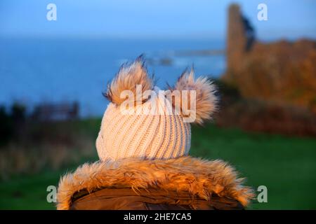 Dunure, Ayrshire, Schottland, Großbritannien. Eine Frau am Wintertag sitzt mit dem Rücken zur Kamera und schaut auf Dunure Castle Stockfoto