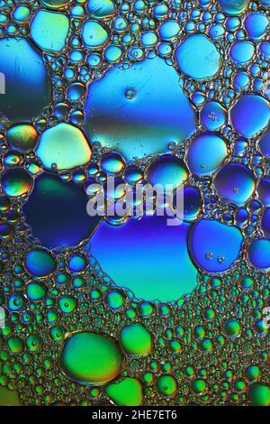 Grün und blau beleuchtete Öltröpfchen schweben auf einer Wasseroberfläche, Makrofotografie Stockfoto
