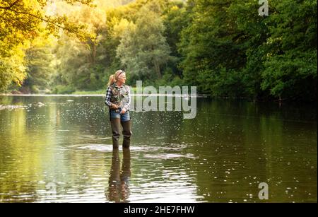 Eine Frau steht im Fluss und fischt mit einer Spinnrute Stockfoto