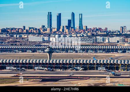 Madrid, Spanien - 31. Dezember 2021: Kontrollturm des Flughafens Adolfo Suarez Madrid-Barajas gegen das Stadtbild mit dem Wolkenkratzer des Geschäftsviertels Cuatro Torres Stockfoto