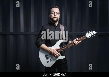 Porträt eines männlichen Gitarristen mit E-Gitarre in schwarzer Kleidung. Rockmusiker Charakter Konzept Stockfoto