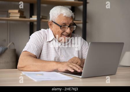 Lächelnder reifer Mann in Brillen, der am Computer arbeitet. Stockfoto