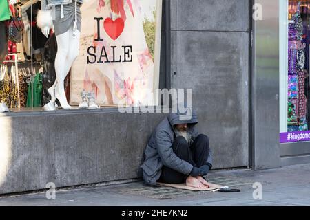 Obdachloser, der auf dem Bürgersteig vor einem Kaufhaus in der Oxford Street, London, Großbritannien, sitzt Stockfoto