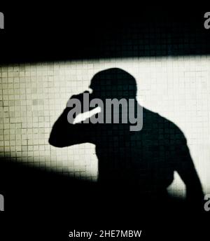 Silhouette eines Mannes an einer Wand, der am Telefon spricht. Stockfoto