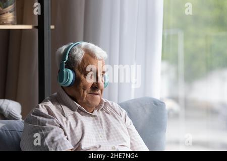 Ein entspannter, lächelnder alter Mann hört Musik in Kopfhörern. Stockfoto
