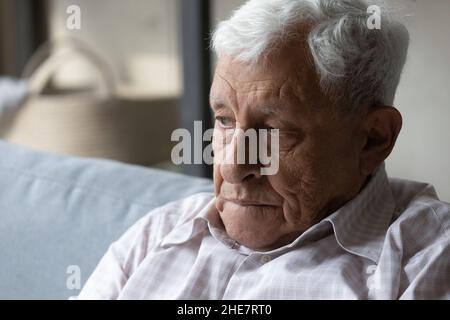 Verloren in negativen Gedanken unglücklicher alter Mann, der auf der Couch saß. Stockfoto