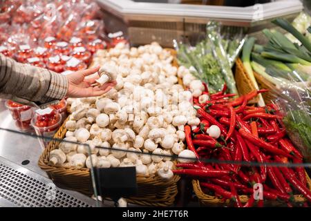 Die Frau wählt in der Gemüseabteilung des Supermarkts Champignons. Mädchen nimmt Pilze aus der Schachtel Stockfoto