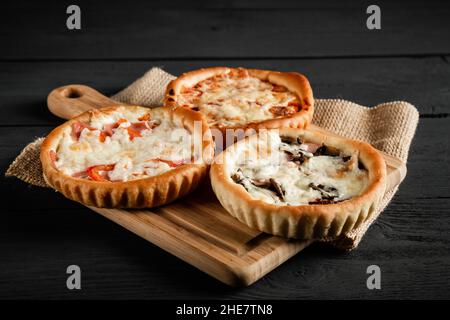 Leckere Pizza auf schwarzem Holzhintergrund. Rustikaler Stil. Mit einem Kopierbereich. Stockfoto