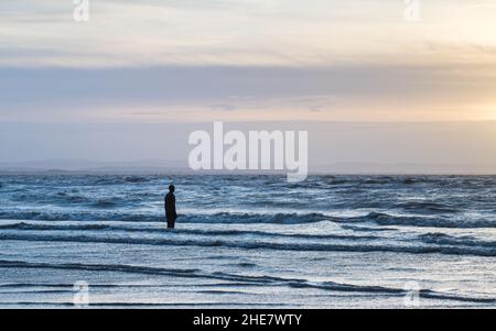 Einer der Iron Men, aus dem Antony Gormley's Another Place, sieht an einem Abend im Januar 2022 die Wellen an den Strand um ihn herum brechen. Stockfoto