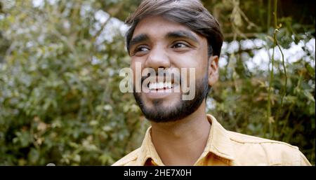 Flacher Fokus eines jungen hübschen indischen Mannes auf Bäume in einem Park Stockfoto