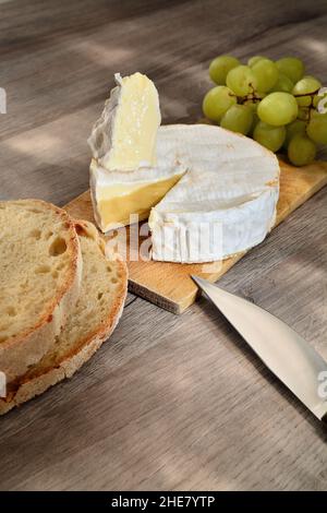 Französischer Camembert der Normandie serviert auf Holzschneidebrett mit Trauben und Brotscheiben. Stockfoto