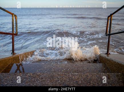 Strom erzeugende Windmühlen in der Nordsee Wellen brechen über Felsen der Meeresabwehr in Skegness, Lincolnshire, Großbritannien Stockfoto