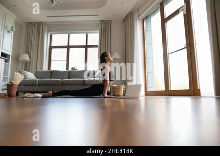 Ruhige Frau, die zu Hause Yoga praktiziert und Online-Videounterricht konsultiert Stockfoto