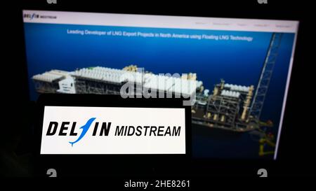 Person, die das Smartphone mit dem Logo des US-amerikanischen LNG-Energieunternehmens Delfin Midstream LLC auf dem Bildschirm vor der Website hält. Konzentrieren Sie sich auf die Telefonanzeige. Stockfoto