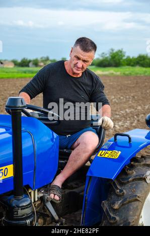 Cherson Oblast, Ukraine - 29. Mai 2021: Ein älterer Landwirt sitzt und fährt einen Traktor. Betrieb eines kleinen Agrarunternehmens. Landwirtschaft. Lockern, Landanbau Stockfoto