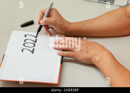 Hand einer älteren Frau, die 2022 in ein Tagebuch schreibt. Vorlage für das neue Jahr 2022, Kopierbereich Stockfoto