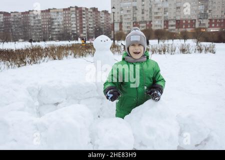 Glücklicher Junge steht im snowcastle und spielen Schneeballspiel im Winterpark Stockfoto