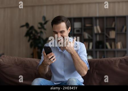 Aufgeregter Mann, der auf den Telefonbildschirm schaute und den Daumen nach oben zeigte Stockfoto
