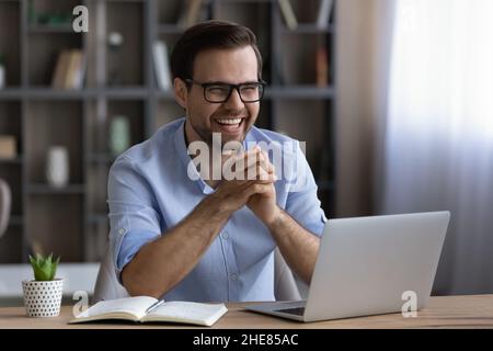 Lachender, fröhlicher Geschäftsmann in einer Brille, der am Schreibtisch sitzt Stockfoto