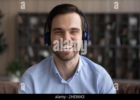 Ein lächelnder Mann mit Kopf-Aufnahme in kabellosen Kopfhörern chattet online Stockfoto