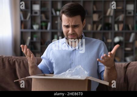 Kopf geschossen unglücklich unzufrieden Mann beim Öffnen Paket zu Hause Stockfoto