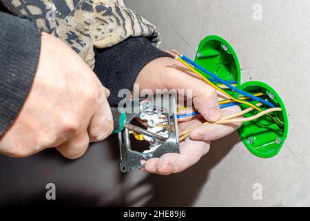 Ein Elektriker installiert eine Steckdose in eine Trockenwand. Durchführung der elektrischen Verdrahtung zum Haus. Stockfoto