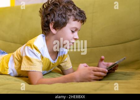 Junge in gelb-weißem T-Shirt spielt begeistert ein Spiel auf einem Tablet Stockfoto