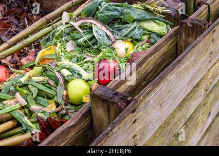 Stapel von Obst- und Gemüseabfällen in hausgemachtem Holzkompostbehälter im Garten, selektiver Fokus Stockfoto