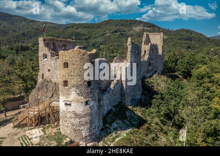 Luftaufnahme der unter Restaurierung mittelalterlichen Burg Reviste über dem Fluss Hron (Garam) in der Slowakei mit Bergfried, kreisförmigem Torturm, ruinierten gotischen Pala Stockfoto