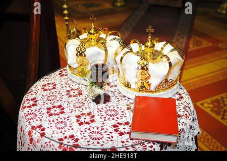 Nahaufnahme von zwei Hochzeitskronen und einem Glas Wein auf dem Tisch in der Kirche Stockfoto