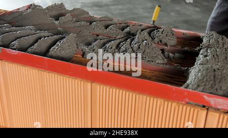 Bauarbeiter, der rohen Zement mit einer Kelle und einem speziellen Rahmen verlegt. Nahaufnahme des Rohmörtels, der auf Keramikblöcke gelegt wird. Stockfoto