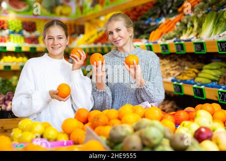 Glückliches Teenager-Mädchen mit Mutter hält reifen Orangen in greengrocery speichern Stockfoto