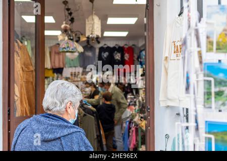 Eine nicht identifizierbare ältere Frau mit einer Maske geht als maskierte Familiengeschäfte in einem Souvenirladen in Zahara de la Sierra, Spanien, ein. Stockfoto