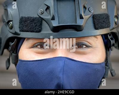 Weibliche taktische Motorrad-Polizist mit Gesichtsmaske und Schutzhelm sieht mit lächelnden braunen Augen und Augen-Make-up auf den Betrachter. Stockfoto