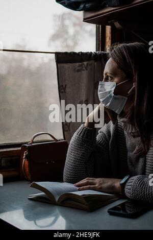 Eine junge Frau in medizinischer Maske reist allein mit dem Zug. Treffen von Vorsichtsmaßnahmen Stockfoto