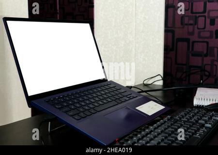 Ein Laptop mit leerem weißen Bildschirm auf dem Schreibtisch, ein Modell. Laptop-Computer auf Holztisch im Wohnzimmer Stockfoto