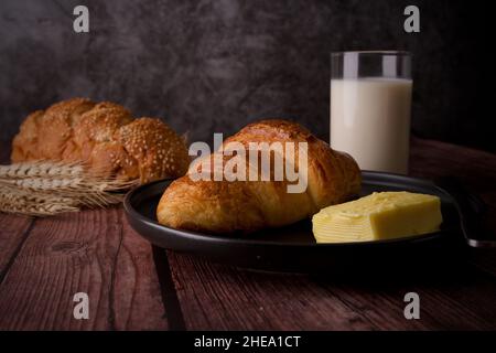 Leckeres Frühstück Croissant mit Butter auf einem Holztisch mit Glasmilch. Stockfoto