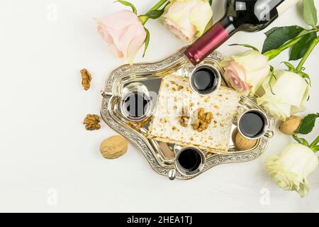 Draufsicht auf ein silbernes Tablett mit Matza, Walnüssen und Rotwein in silbernen Gläsern. rosen auf weißem Hintergrund. Das Konzept des jüdischen Passahfestes Stockfoto