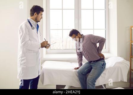 Junger männlicher Patient beschwert sich beim Arzt über starke Rückenschmerzen während des Krankenhausaufenthalts. Stockfoto