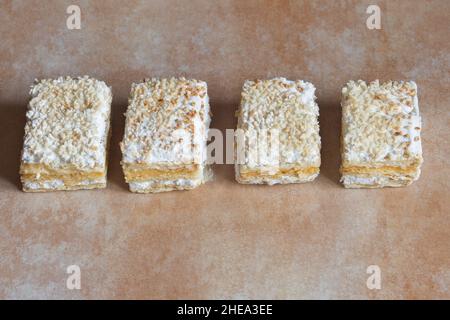 Eine Reihe von einzelnen Portionen Millefeuille aus Blätterteig und gefüllt mit Backcreme und Baiser mit gerösteten gehackten Mandeln und Zucker. Stockfoto