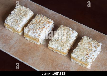 Mehrere einzelne Portionen Kruste in einer Reihe auf einem abstrakt strukturierten, pastellfarbenen Tablett. Traditionelles Dessert aus süßem Blätterteig mit Creme. Stockfoto