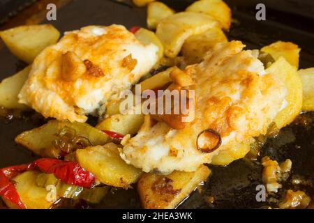 Nahaufnahme von Kabeljau auf einem Backblech, das mit roten Paprika, Kartoffeln und Knoblauch gekocht wird. Fisch und gesunde Lebensmittel. Stockfoto