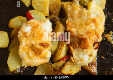 Ansicht eines Backblech mit mit rotem Paprika, Kartoffeln und Knoblauch gekochtem Seehecht von oben. Vorbereitung, einfaches Kochen. Stockfoto